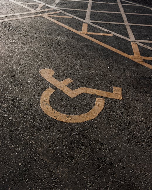 A close-up view of a designated disabled parking space on an asphalt surface, featuring a yellow wheelchair symbol painted directly onto the ground. The parking bay is outlined with yellow lines, with a portion of the adjacent lane visible in the background. The surface appears textured and well-maintained, suitable for vehicular access and parking during home relocation or furniture transport activities. This image is relevant to house removals and moving services provided by Man with Van The Burroughs, particularly in facilitating accessible parking arrangements near properties in NW4 during the loading and unloading phases of a move on the street accessed for the move detailed in The Burroughs moving guide.