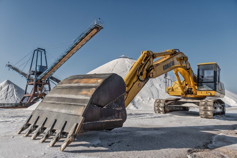 A yellow front-end loader equipped with a large bucket attachment is clearing snow on a flat, snow-covered landscape under a partly cloudy sky. The machine is actively scooping and pushing snow, creating a pile in front of its bucket. The surrounding area is vast and open, with no other structures or vehicles visible, indicating an outdoor environment suitable for heavy-duty snow removal or land clearing. Images of equipment like this are relevant to professional removals and transportation services, especially in regions prone to snow. Man with Van The Burroughs offers such services including handling heavy items and home relocations, which may involve outdoor logistics and equipment use during winter months.